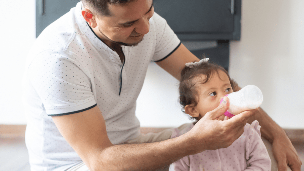 a person feeding a baby while sitting on the floor