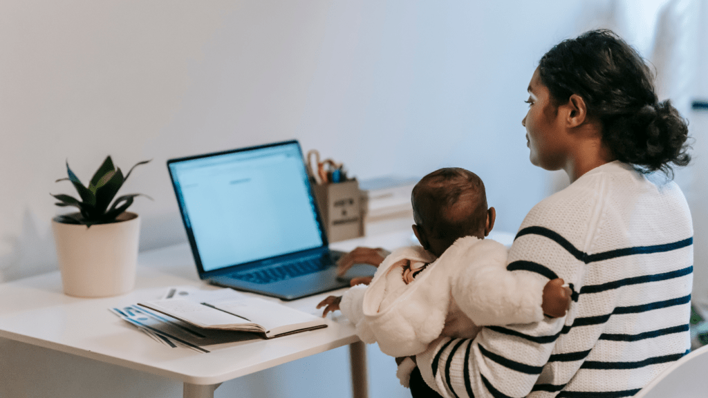 a person holding a baby and sitting at a desk with a laptop