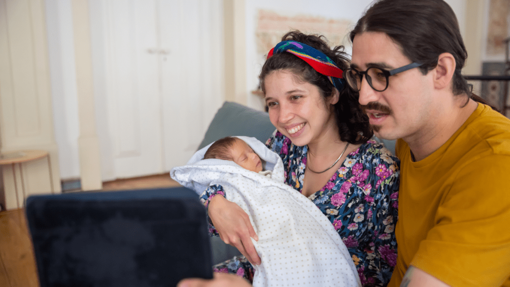 Two individuals holding a baby while looking at a tablet