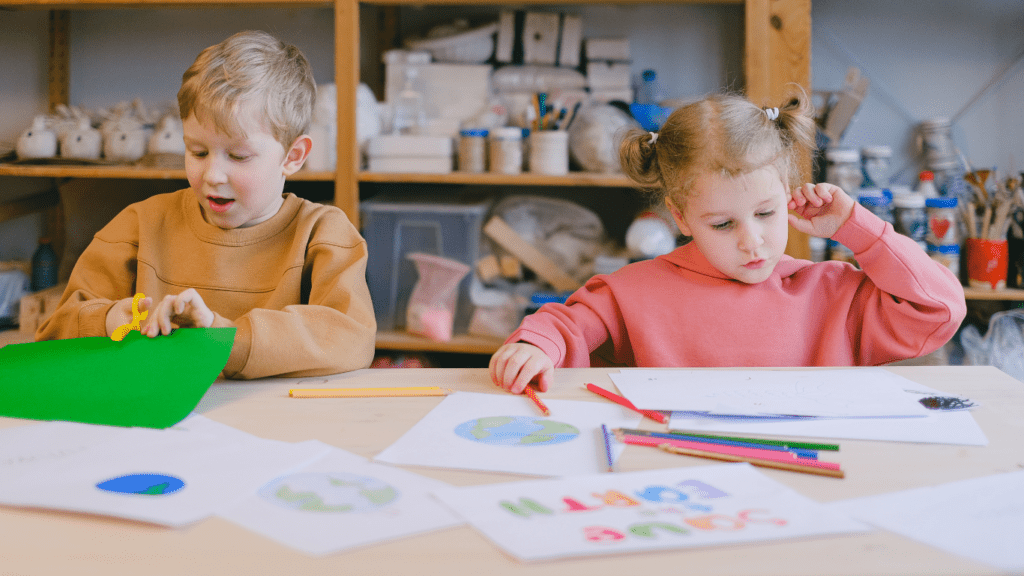 two children sitting at a table with paper and pencils