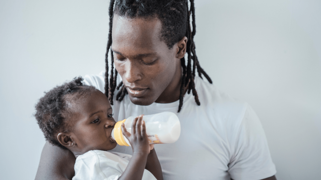 a person feeding a baby while sitting on the floor