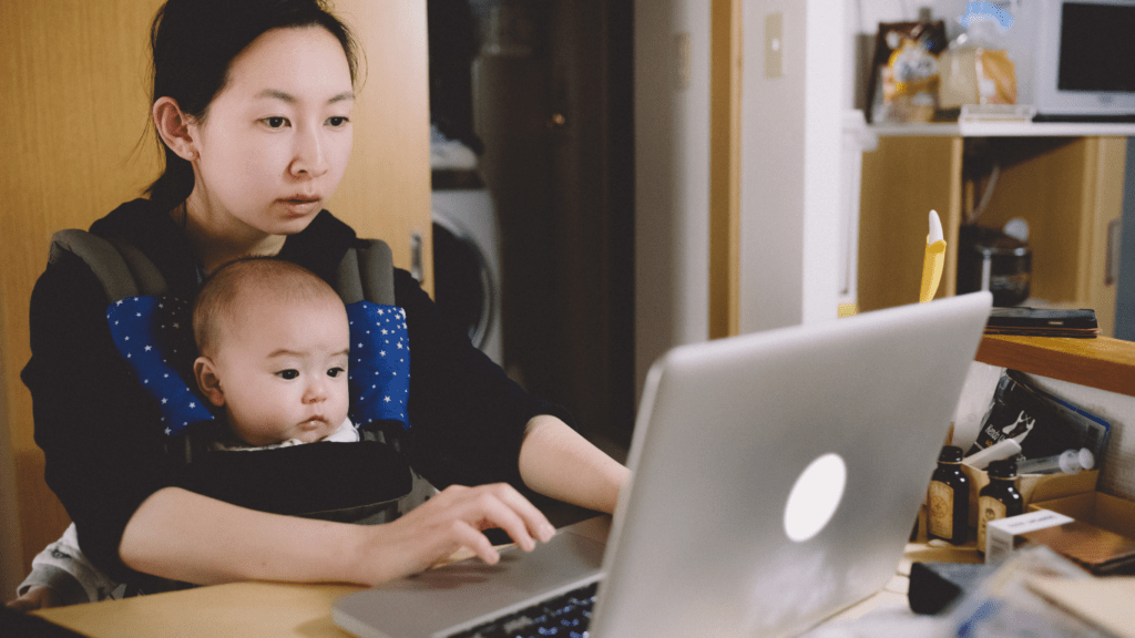 a person holding a baby and sitting at a desk with a laptop