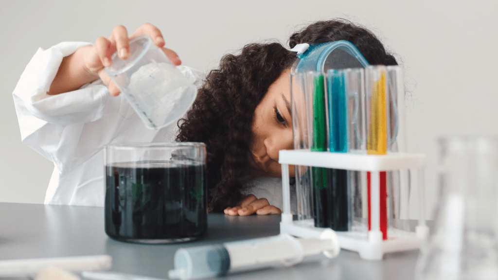 a person in a lab coat and goggles looking at a green liquid