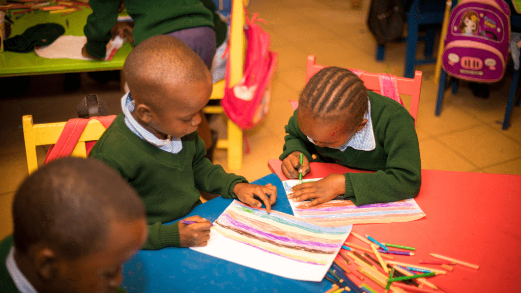 two children sitting at a table with paper and pencils